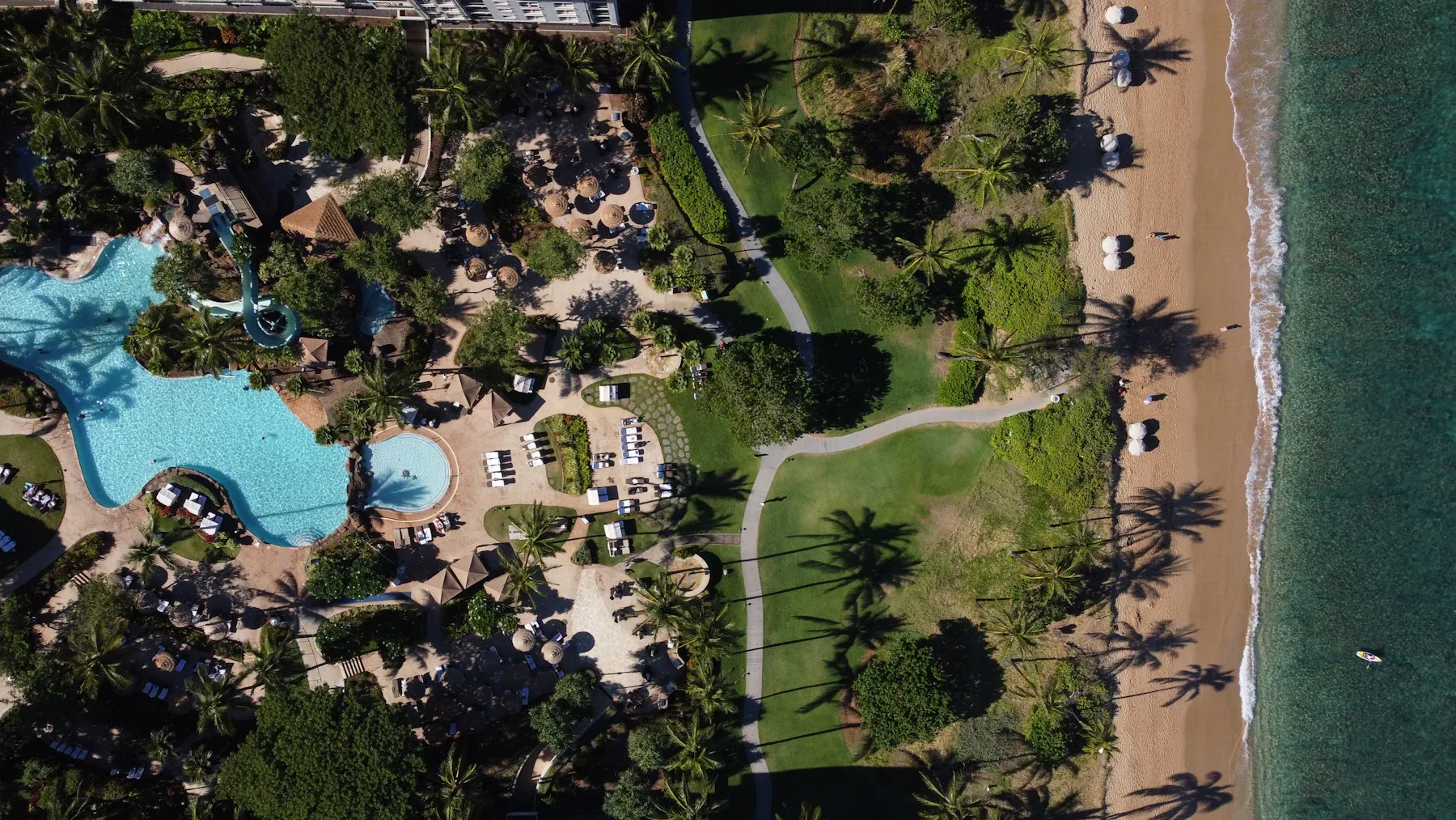 Vista aérea de um resort à beira-mar, com piscinas, jardins e acesso à praia em Kaanapali, Havaí.